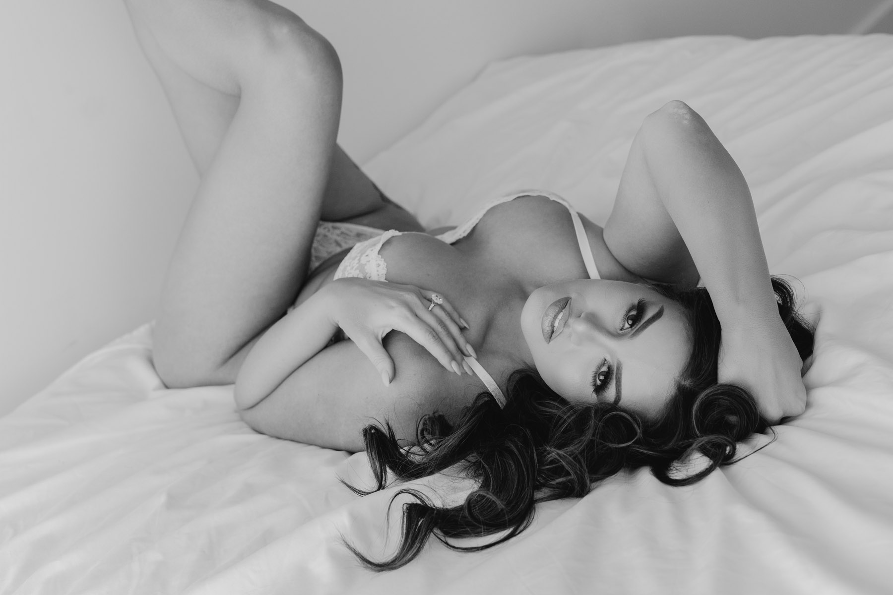 Brunette in lace photographed in monochrome on white sheets