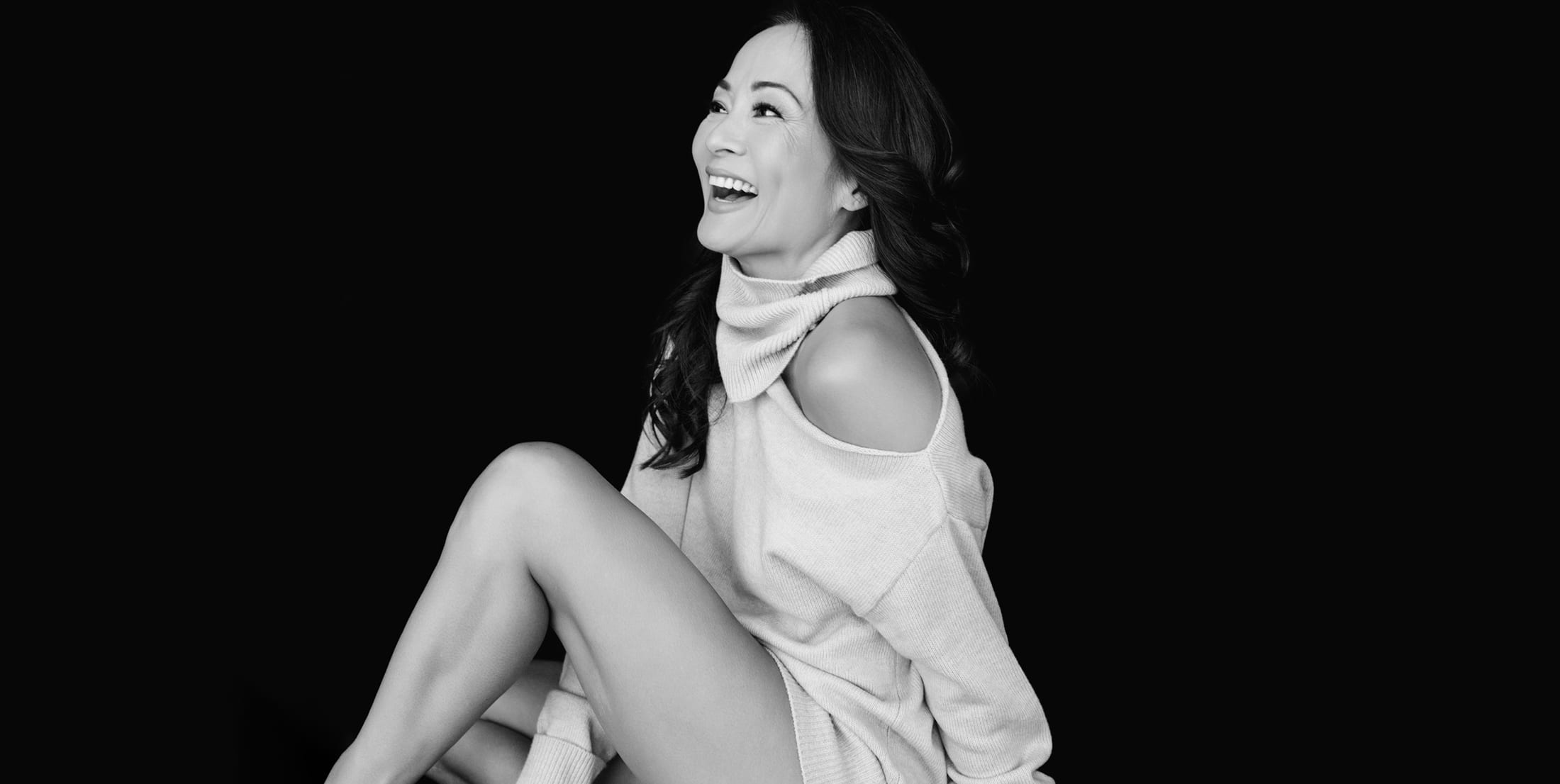 Black-and-white editorial portrait of a woman seated and laughing in a soft cold-shoulder sweater — signature image for J Renee Studios, modern boudoir and portrait photography in Boise and Las Vegas